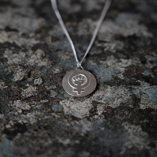 Silver pendant with feminist fist symbol, on slate background