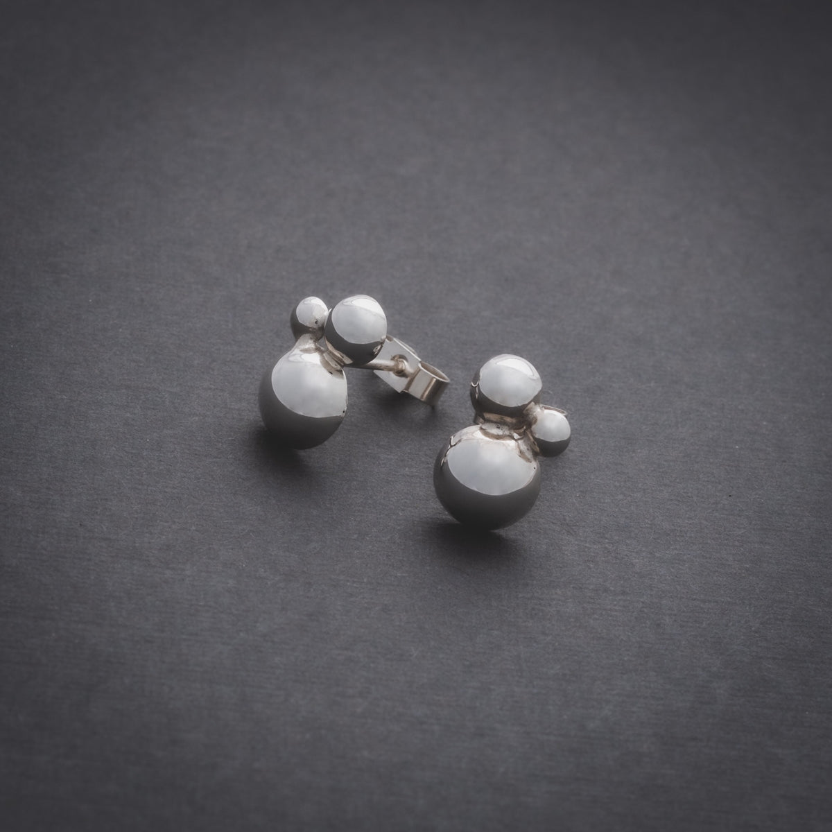 Product shot of silver stud earrings made of three domes