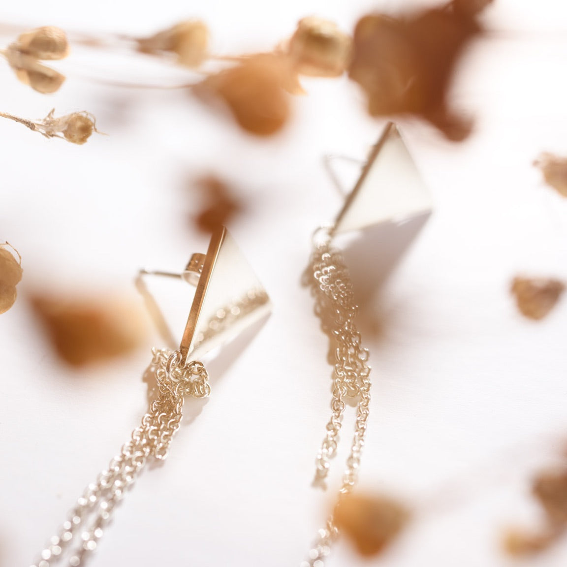 Close up, gauzy shot of triangle stud earrings with chain tassels